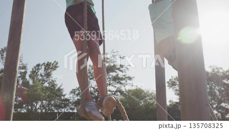 Climbing boy wearing shirt and shorts gripping thick ropes on wooden posts at outdoor playground Climbing boy wearing shirt and shorts gripping thick ropes on wooden posts at outdoor playground 135708325