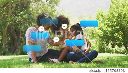 Chatting grandmother mother and daughter sitting on grassy park lawn, with digital speech bubbles Chatting grandmother mother and daughter sitting on grassy park lawn, with digital speech bubbles 135708398