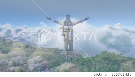 Standing hiker in shorts and boots extending arms toward clouds on mountain ridge with backpack mat 135708430