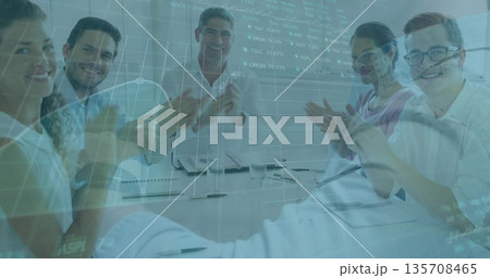 Clapping professionals applauding around boardroom table, with notebooks and digital charts overlay 135708465