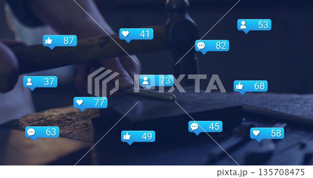 Female metalworker wearing dark apron hammering rod on block in workshop, with notification icons Female metalworker wearing dark apron hammering rod on block in workshop, with notification icons 135708475