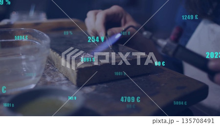 Heating metal with torch on firebrick at workbench wearing protective apron with currency symbols 135708491