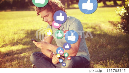 Sitting man wearing dotted shirt scrolling smartphone in park, with floating thumbs up icons Sitting man wearing dotted shirt scrolling smartphone in park, with floating thumbs up icons 135708545