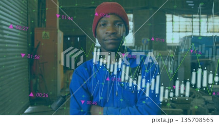 Standing technician wearing red cap and blue coverall in workshop, with financial data overlays Standing technician wearing red cap and blue coverall in workshop, with financial data overlays 135708565
