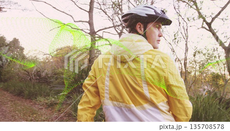 Exploring cyclist with helmet, yellow windbreaker on woodland trail, green mesh overlay, copy space 135708578