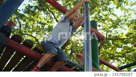 Climbing child wearing striped t-shirt, shorts grabbing silver pole at park under adult hand 135708587