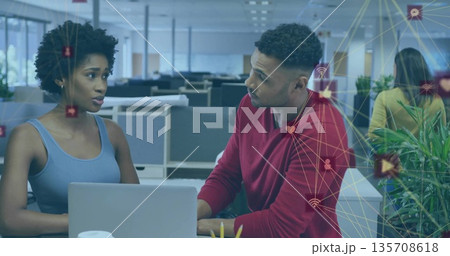 Discussing woman and male colleague collaborating at office desk, with laptop and network icons Discussing woman and male colleague collaborating at office desk, with laptop and network icons 135708618