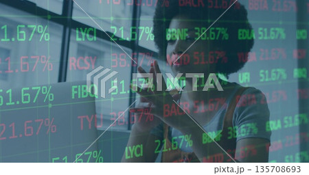 Standing analyst in brown overalls examining stock tickers on touchscreen in office with laptop Standing analyst in brown overalls examining stock tickers on touchscreen in office with laptop 135708693