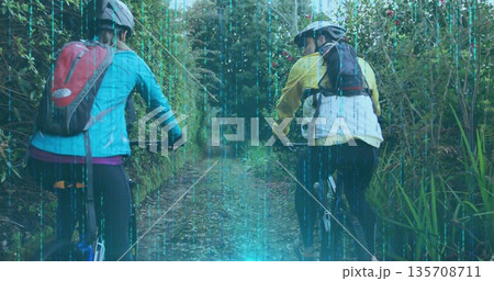 Pedaling friends wearing helmets and jackets along woodland trail, with mountain bikes and packs Pedaling friends wearing helmets and jackets along woodland trail, with mountain bikes and packs 135708711