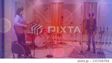 Three musicians recording song in studio, wearing headphones with acoustic guitar and red drum kit 135708769