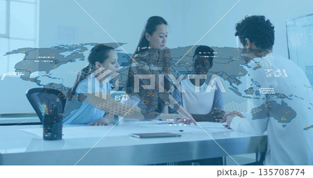 Businesswomen reviewing documents and pointing in boardroom, with tablet and world map overlay 135708774