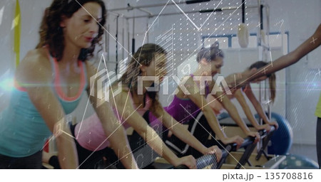 Leaning six women pushing reformer carriages in pilates studio, with exercise ball data charts 135708816