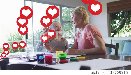 Mother and daughter painting together in home craft area, with colorful paint jars and heart icons 135709516