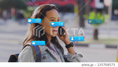 Smiling woman holding smartphone viewing social media notifications on sidewalk wearing smartwatch 135709573