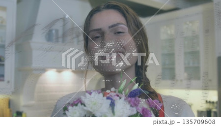 Smiling woman wearing sweater and red apron holding bouquet in white kitchen, with glitch overlay 135709608