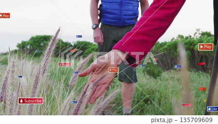Reaching hiker woman in red top brushing grass plumes at meadow, with overlay subscribe like icons 135709609