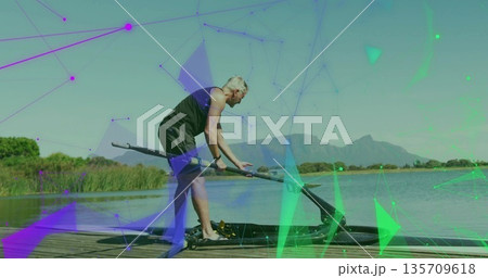 Senior man in sleeveless top adjusting oar into scull oarlock on pier beside lake, polygon overlay Senior man in sleeveless top adjusting oar into scull oarlock on pier beside lake, polygon overlay 135709618