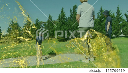 Swinging man hitting bunker shot with golf club on fairway, golfers watching under spark overlay Swinging man hitting bunker shot with golf club on fairway, golfers watching under spark overlay 135709619