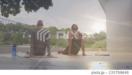 Practicing two men holding upward-facing dog pose on balcony, with yoga mats towels water bottles 135709648