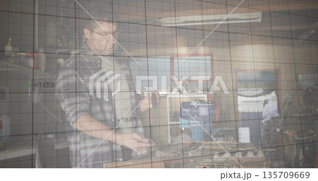 Mechanic wearing plaid shirt and glasses examining engine block in garage workshop, copy space 135709669