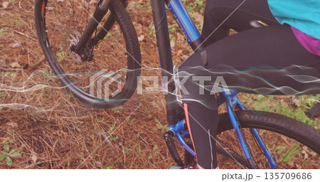 Adult cyclist riding on forest trail in tight athletic wear, with blue bicycle and waveform overlay 135709686