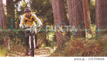 Cyclist wearing helmet, yellow jacket riding mountain bike on pine trail, with digital overlay 135709688