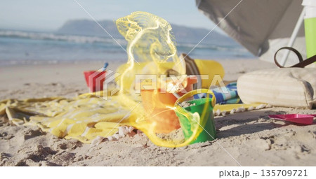 Arranging colorful sand buckets and shovel on sunny beach shore, with striped towel and cooler bag 135709721