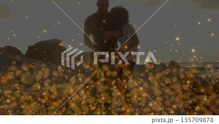 Walking couple along sunset beach with large rocks, with man checking watch and bokeh lights Walking couple along sunset beach with large rocks, with man checking watch and bokeh lights 135709878