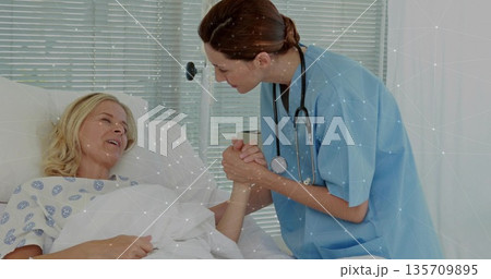 Holding patient hand, nurse wearing scrubs and stethoscope comforting patient lying in ward in gown Holding patient hand, nurse wearing scrubs and stethoscope comforting patient lying in ward in gown 135709895