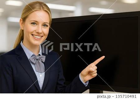 現代的なオフィスでモニター画面を指さすスーツ姿のビジネスウーマンがプレゼンや企業研修を表現 135710491