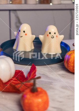 Ghost-themed halloween desserts on blue plate with pumpkins and autumn leaves 135710904