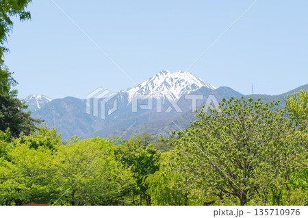 長野県安曇野市　新緑の木々の間から望む残雪の常念岳と青空 135710976