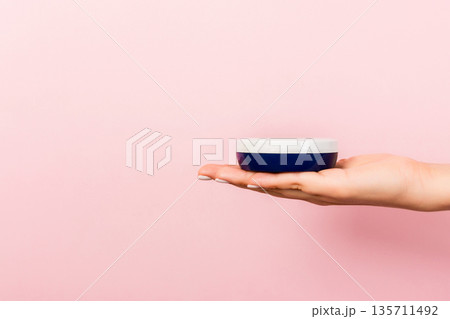 Female hand holding cream bottle of lotion isolated. Girl give jar cosmetic products on pink background Female hand holding cream bottle of lotion isolated. Girl give jar cosmetic products on pink background 135711492