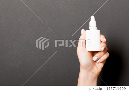 Female hands hold medicine bottle nose spray on Black background isolation 135711499