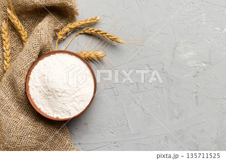 Flat lay of Wheat flour in wooden bowl with wheat spikelets on colored background. world wheat crisis Flat lay of Wheat flour in wooden bowl with wheat spikelets on colored background. world wheat crisis 135711525