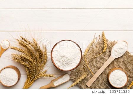 Flat lay of Wheat flour in wooden bowl with wheat spikelets on colored background. world wheat crisis Flat lay of Wheat flour in wooden bowl with wheat spikelets on colored background. world wheat crisis 135711526
