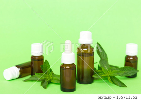 Natural Mint Essential Oil in a Glass Bottle. organic cosmetics with herbal extracts of mint on colored background Natural Mint Essential Oil in a Glass Bottle. organic cosmetics with herbal extracts of mint on colored background 135711552