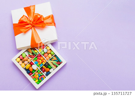 Set of different sweet candy in a paper box with a satin ribbon on a colored background. Holiday concept 135711727