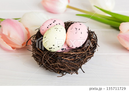 Happy Easter. Easter eggs in nest on colored table with tulip. Natural dyed colorful eggs background top view with copy space Happy Easter. Easter eggs in nest on colored table with tulip. Natural dyed colorful eggs background top view with copy space 135711729
