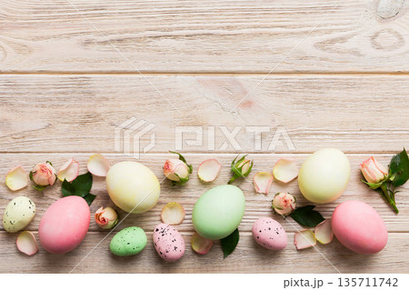 Happy Easter. Easter eggs on colored table with yellow roses. Natural dyed colorful eggs background top view with copy space Happy Easter. Easter eggs on colored table with yellow roses. Natural dyed colorful eggs background top view with copy space 135711742