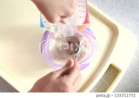 baby food and nutrition concept - mother hands with jar, spoon and bowl preparing cereal from powder close up 135711772
