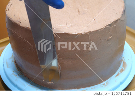 Confectioner woman is smearing cream on sides of cake using spatula, closeup view. culinary, baking and cooking food concept, home cooking 135711781