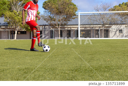 African American man controlling soccer ball near goalpost on turf in red uniform, copy space 135711899