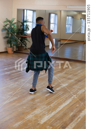 African American man practicing dance moves in studio with mirrored wall, barre and plants 135711905