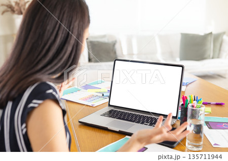 Asian woman working at wooden table in home living room with laptop, swatches, design layouts Asian woman working at wooden table in home living room with laptop, swatches, design layouts 135711944