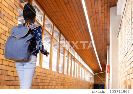 African American child walking down school hall with denim backpack near windows and recycling bins African American child walking down school hall with denim backpack near windows and recycling bins 135711962