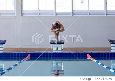 Male swimmer crouching on starting block number eight above turquoise tiled pool lanes Male swimmer crouching on starting block number eight above turquoise tiled pool lanes 135712029