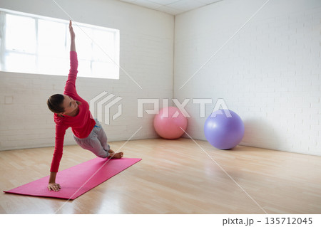 Woman holding side plank on pink yoga mat in studio with pink-purple exercise balls, copy space Woman holding side plank on pink yoga mat in studio with pink-purple exercise balls, copy space 135712045