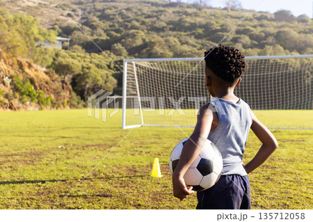African American boy in sportswear holding ball facing net on soccer field near cone, copy space African American boy in sportswear holding ball facing net on soccer field near cone, copy space 135712058