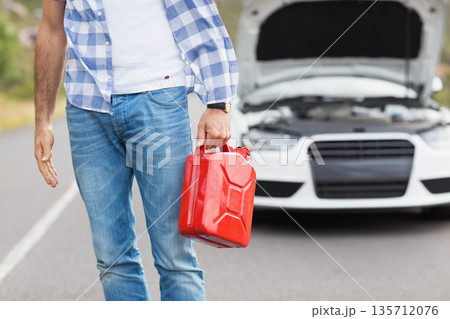 Mid adult male holding red fuel container beside white sedan with open hood on rural road 135712076